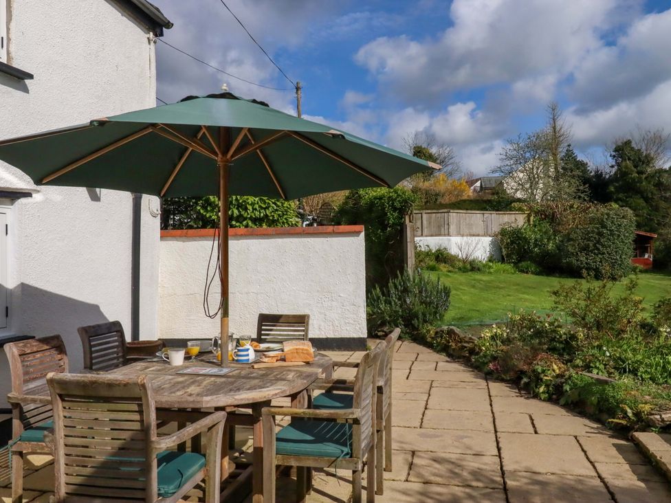 A table with chairs and an umbrella on a patio at Town Farm Cottage in Barnstaple