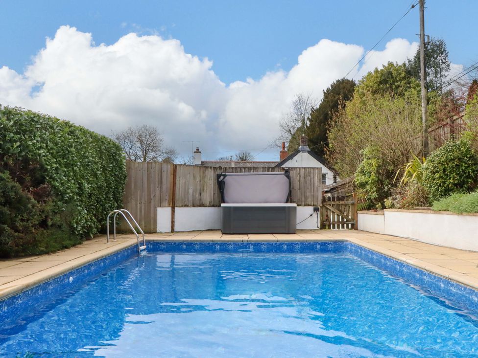 A swimming pool surrounded by decking and hedges at Town Farm Cottage in Barnstaple