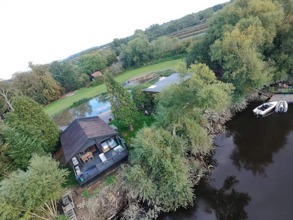 An outdoor view of a house by a river with a boat docked at The Larch House in Farndon