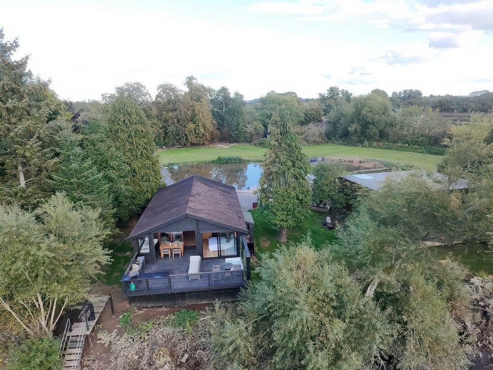 An outdoor view of a house surrounded by trees near a pond at The Larch House Farndon