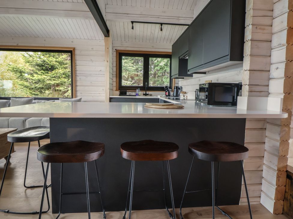 A kitchen with a bar area and three stools at The Larch House in Farndon