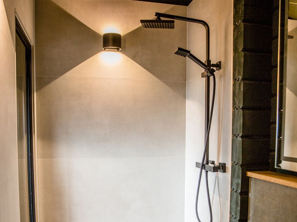 A shower with a black faucet and shower head at The Larch House in Farndon