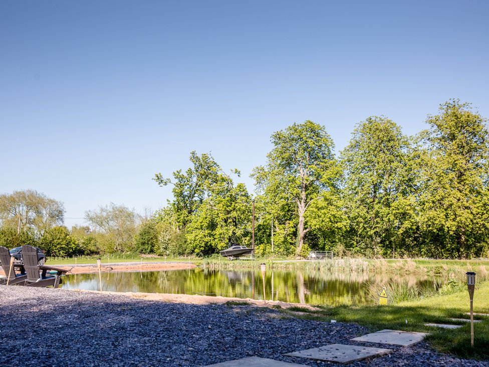 A view of a pond with trees and a boat at The Larch House in Farndon