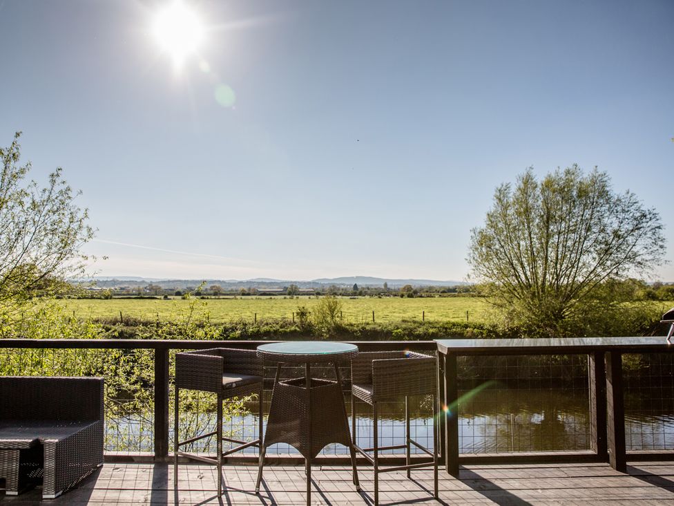 A deck with table and chairs overlooking fields and water at The Larch House in Farndon