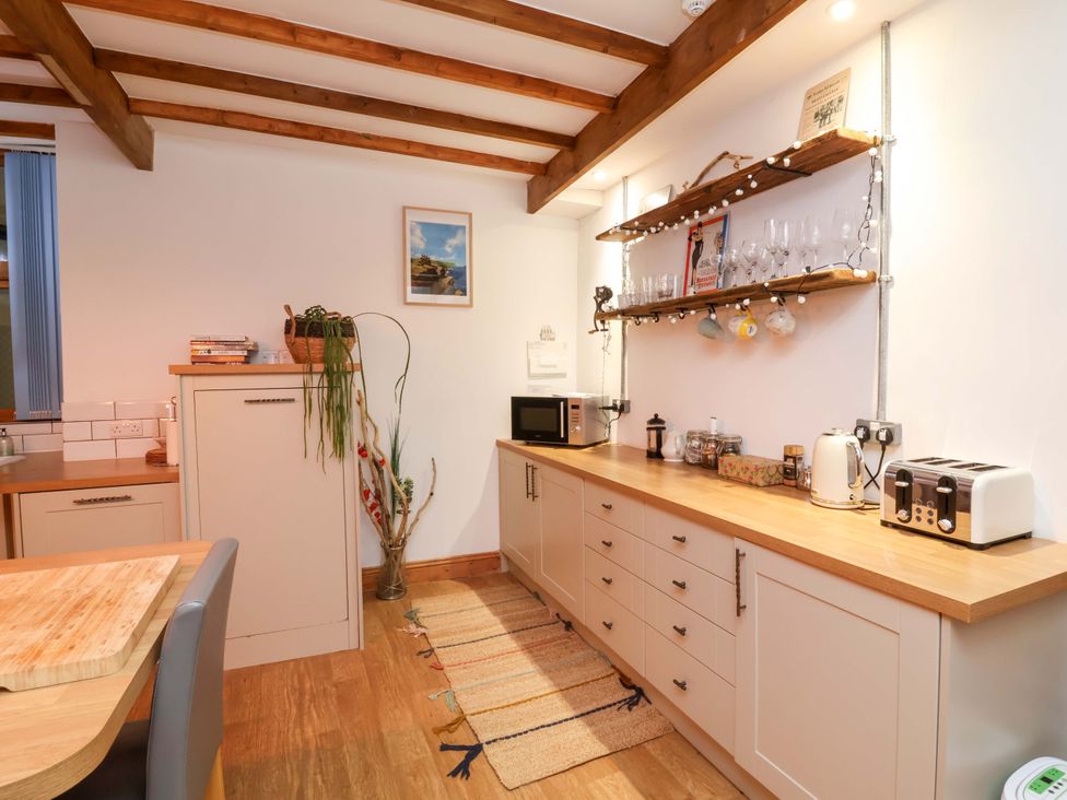 A kitchen with a microwave, kettle, and shelf with glasses at Baywatch (St. David's View) Lynton