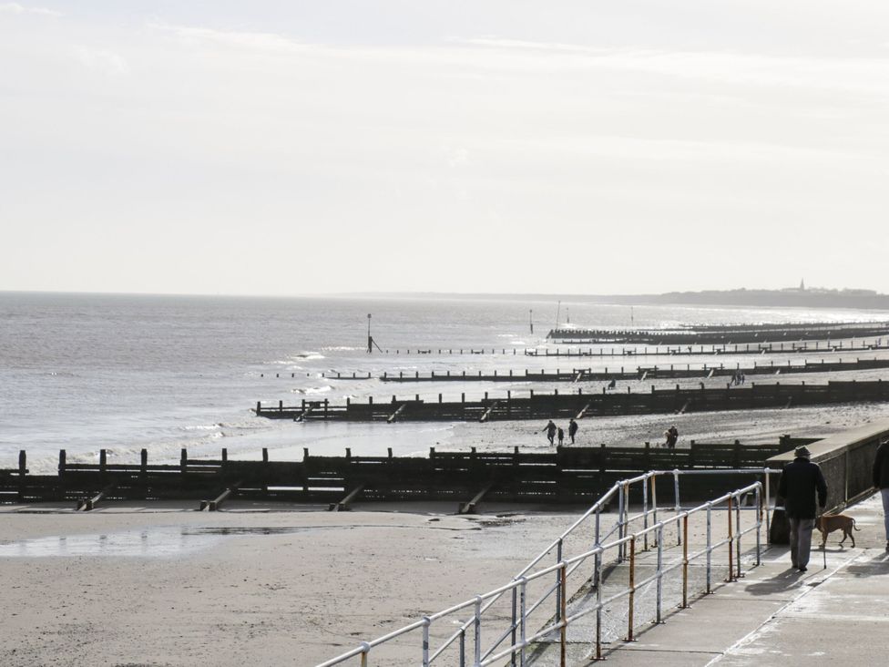 A beach with people walking along a promenade at Meadows Park 4 Great Hatfield near Hornsea