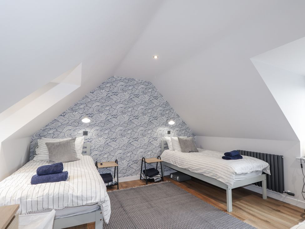 A bedroom with two beds and a patterned wall at Apple Tree Cottage in Cullen