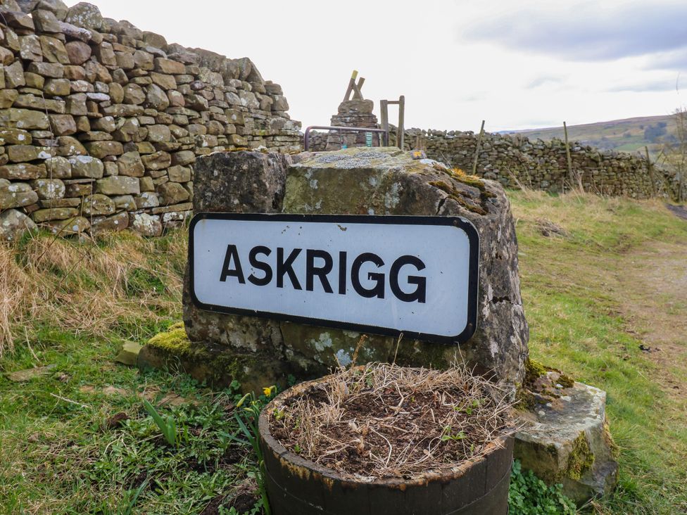 A sign for Askrigg next to a stone wall in a rural area near Askrigg near West Burton