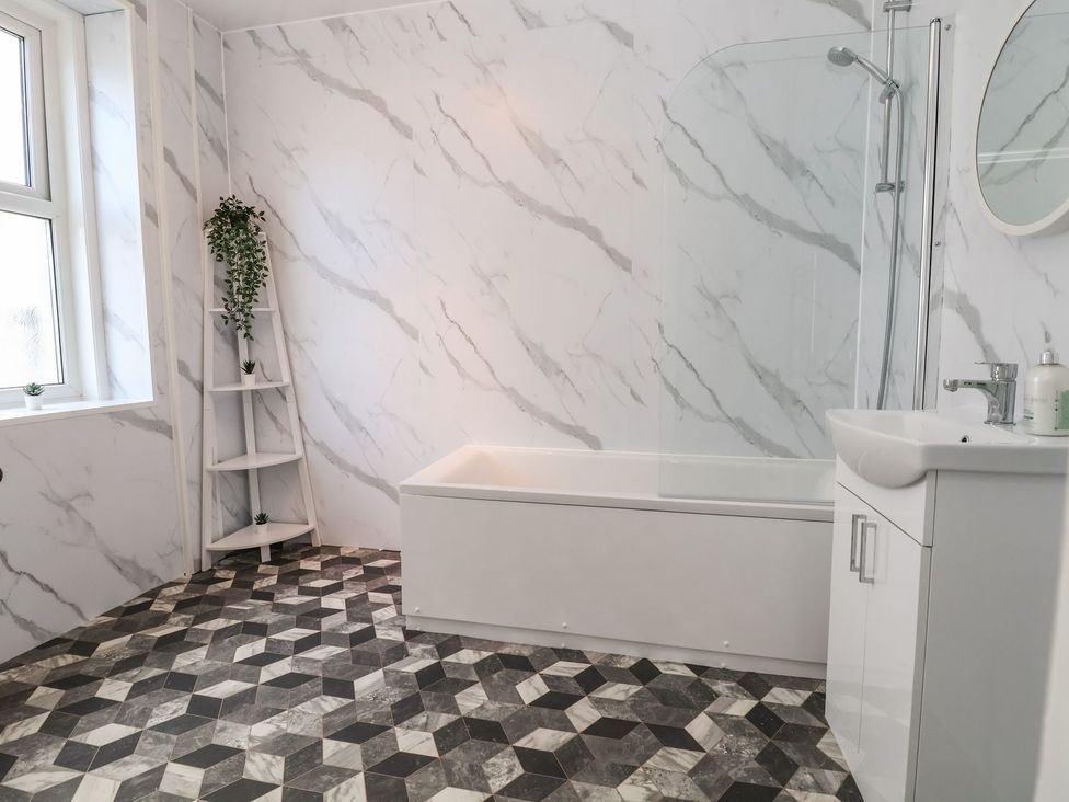 A bathroom with a bathtub, shower, sink, and shelving at Mariners Lee