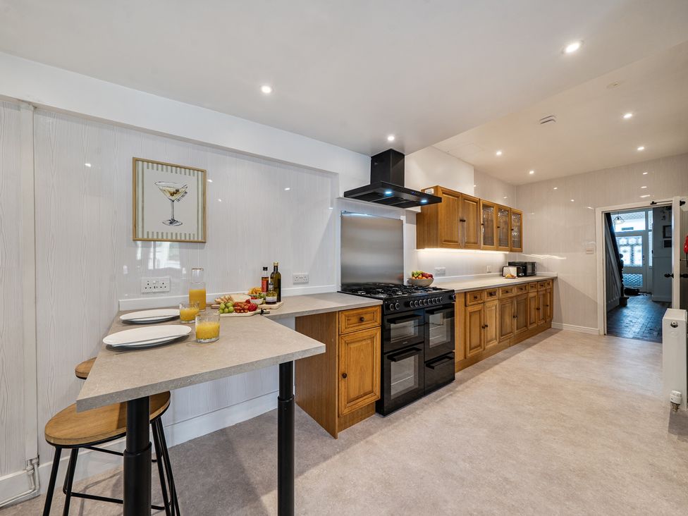 A kitchen with cabinetry, countertop, stove, and bar stools at Clarence House in Llandudno