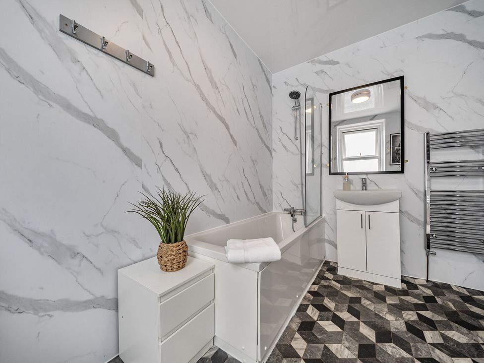 A bathroom with a bathtub, sink, and mirror at Clarence House in Llandudno