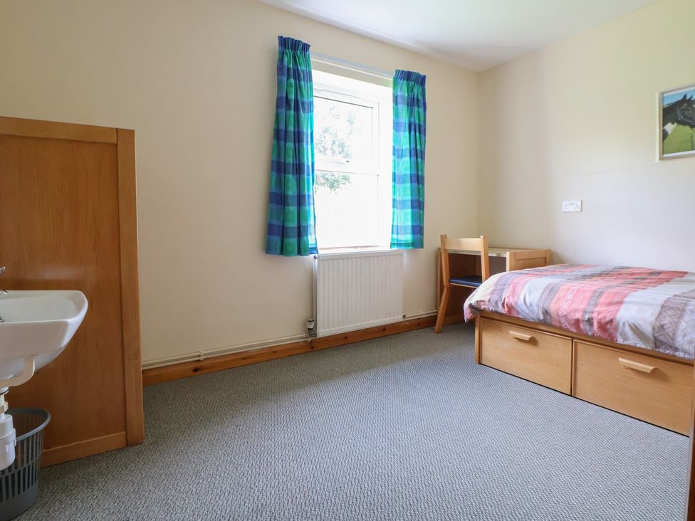 A bedroom with a bed, desk, chair, and sink at Clwyd Special Riding Centre