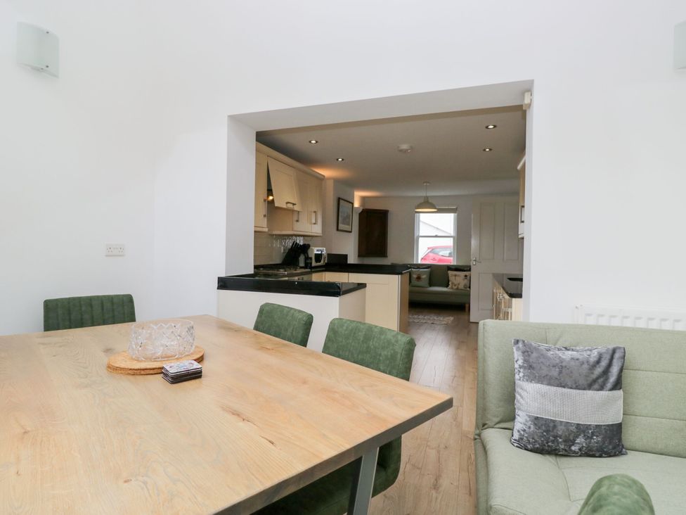 A dining room with a table and chairs looking into a kitchen at Swirl Howe in Keswick