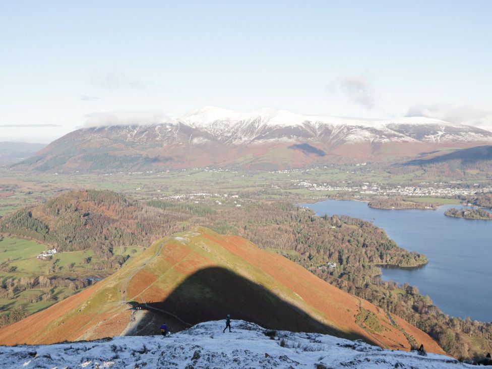 A view of mountains and a lake with hikers in the foreground at Swirl Howe, Keswick