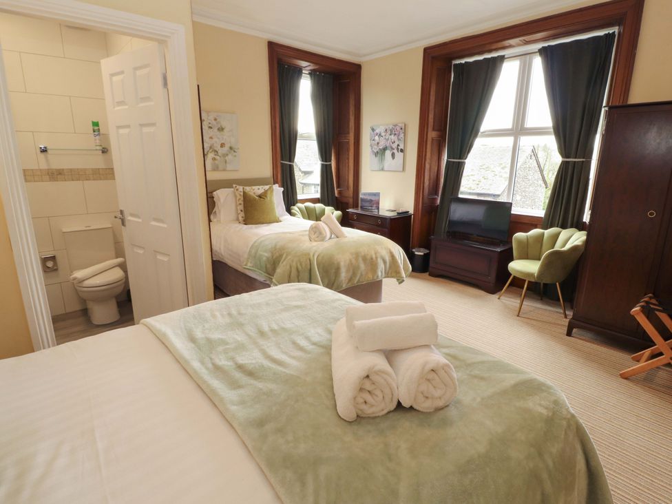 A bedroom with two beds and an armchair at 1 Park Road Windermere
