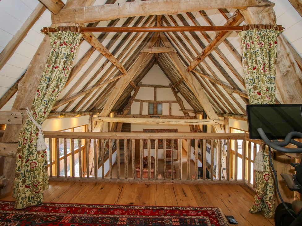 A loft with wooden rafters and a balcony overlooking a sitting area at Crook Barn in Tenbury Wells