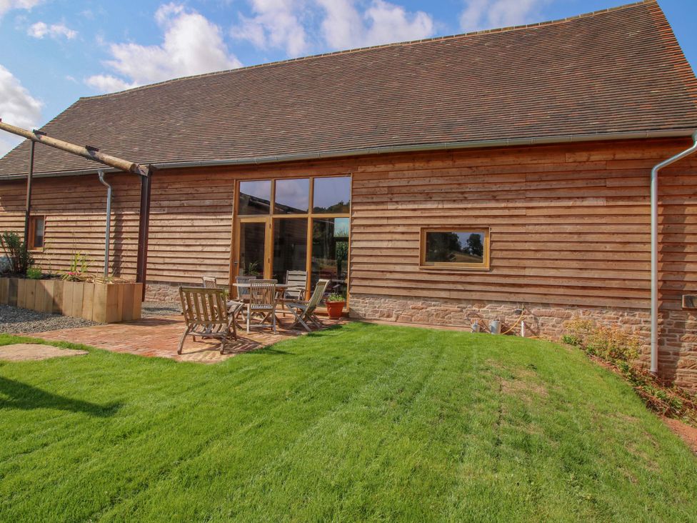 An outdoor seating area with wooden furniture and a lawn at Crook Barn in Tenbury Wells