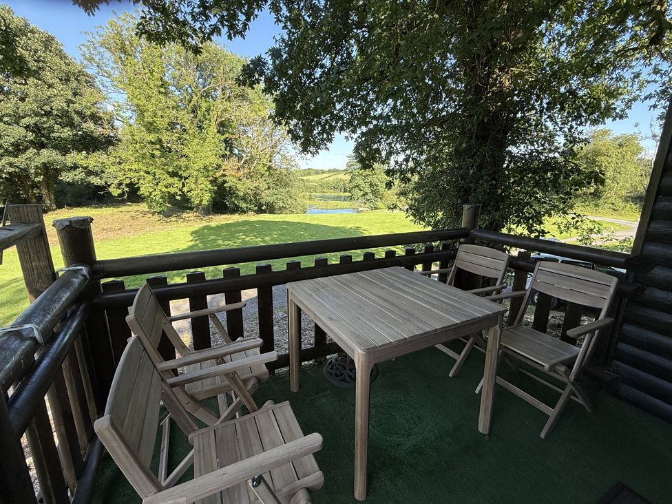 An outdoor seating area with a table and chairs overlooking a pond at Oak Lodge Mynydd Cerrig near Porthyrhyd