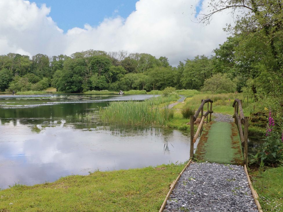 A pond with a bridge and pathway surrounded by trees at Oak Lodge near Mynydd Cerrig