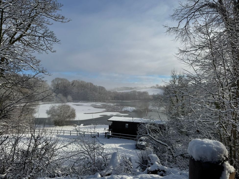 A snowy landscape featuring a lake and a cabin at Ash Lodge near Mynydd Cerrig Porthyrhyd