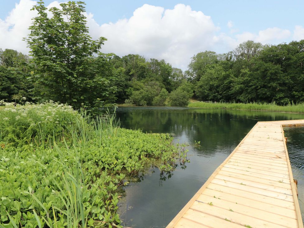 A serene view of water with a wooden walkway and trees at Ash Lodge near Mynydd Cerrig