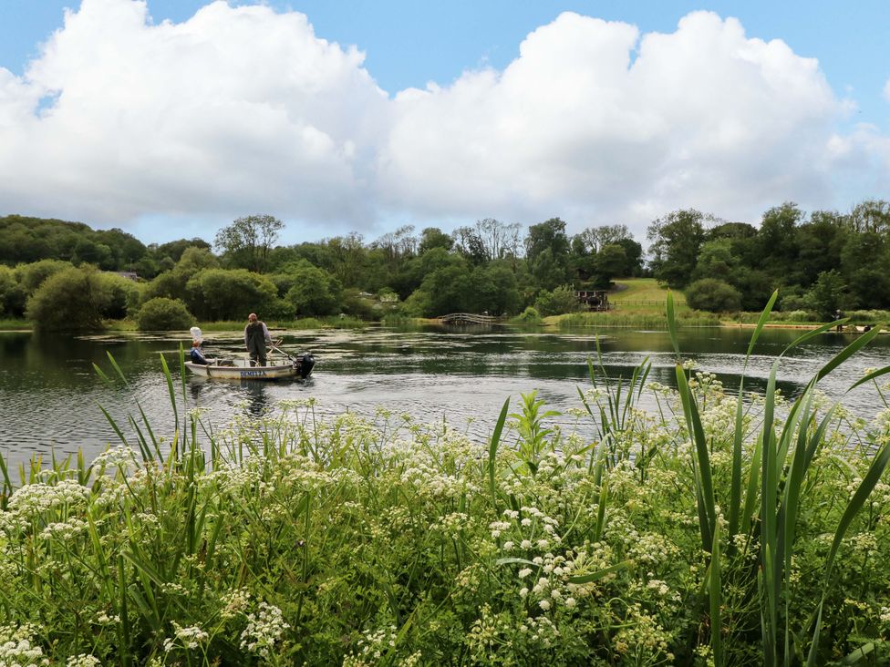 A boat with people on a lake with trees and a bridge at Ash Lodge near Mynydd Cerrig
