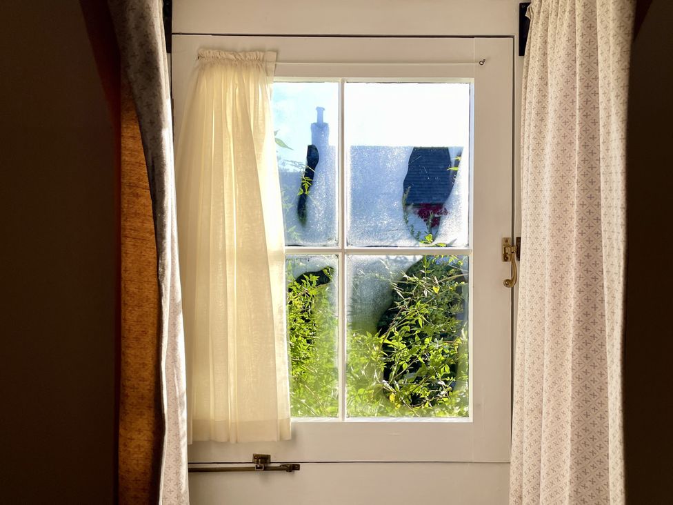 A window with a curtain showing greenery at West Cottage in Myddfai near Llandovery