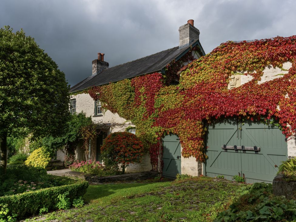 A house with ivy on the walls and green garage doors at West Cottage in Myddfai near Llandovery