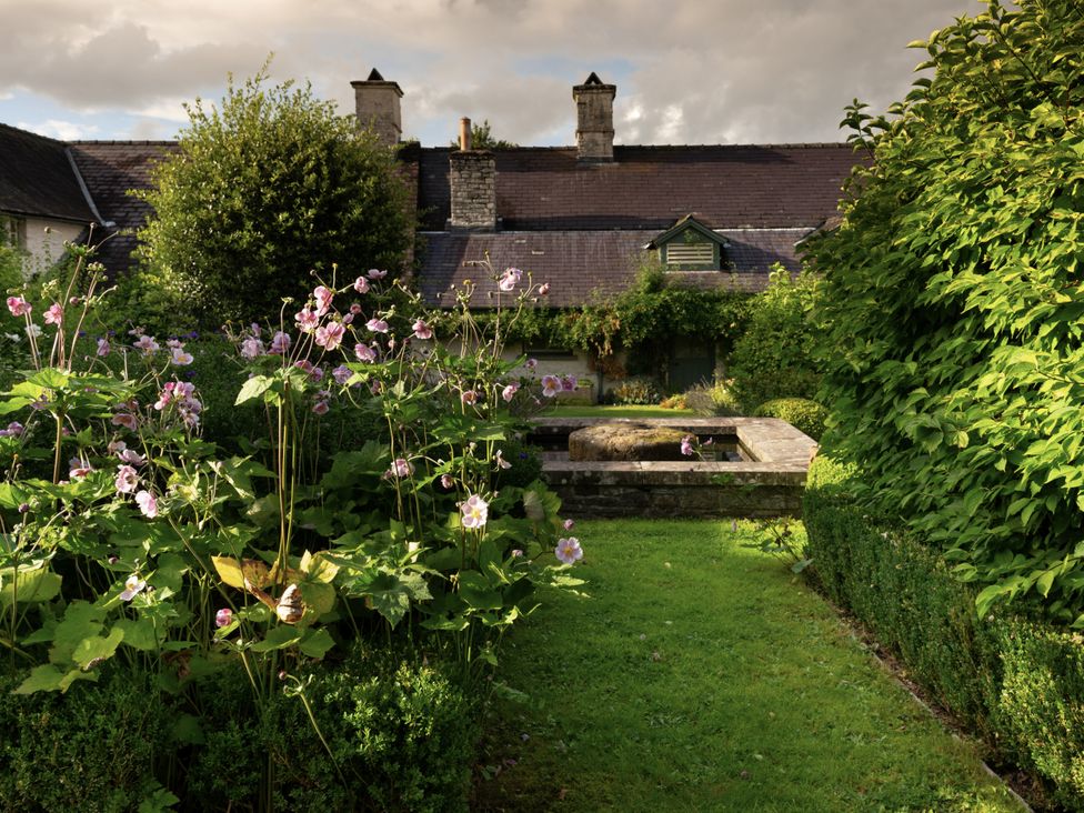 A garden with flowers and a stone fountain at West Cottage Myddfai near Llandovery