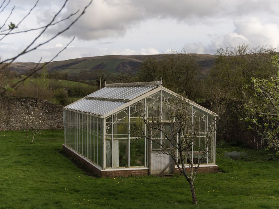 A greenhouse with glass panels in a garden at Gatekeepers Cottage near Llandovery