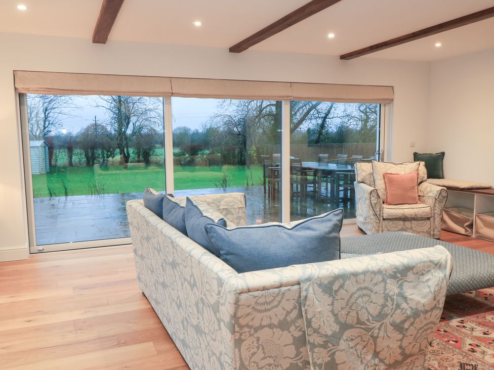 A living room with a sofa and armchair overlooking a garden at Peewit Coach House in Moreton-in-Marsh