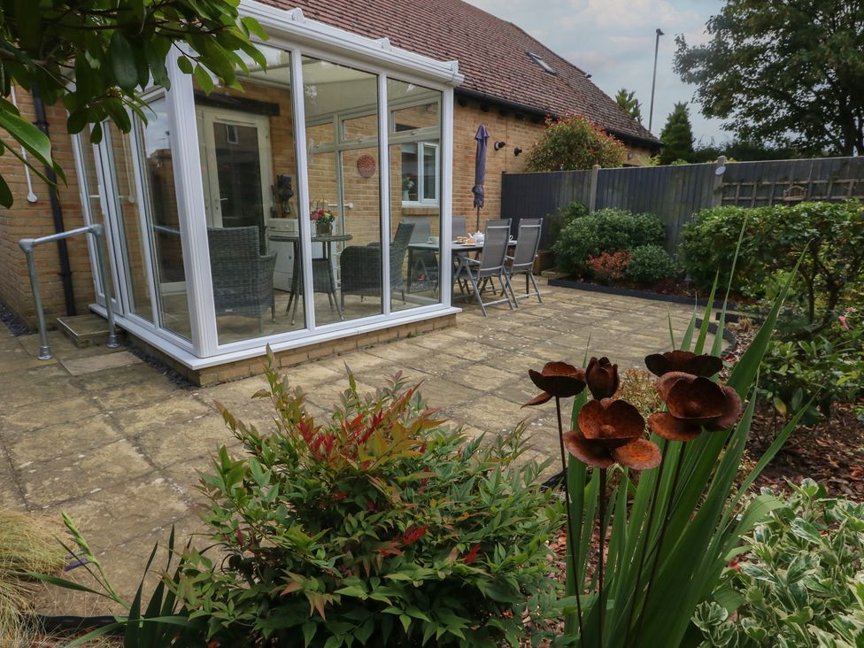 A garden with a glass conservatory and patio seating at June Cottage in Wool