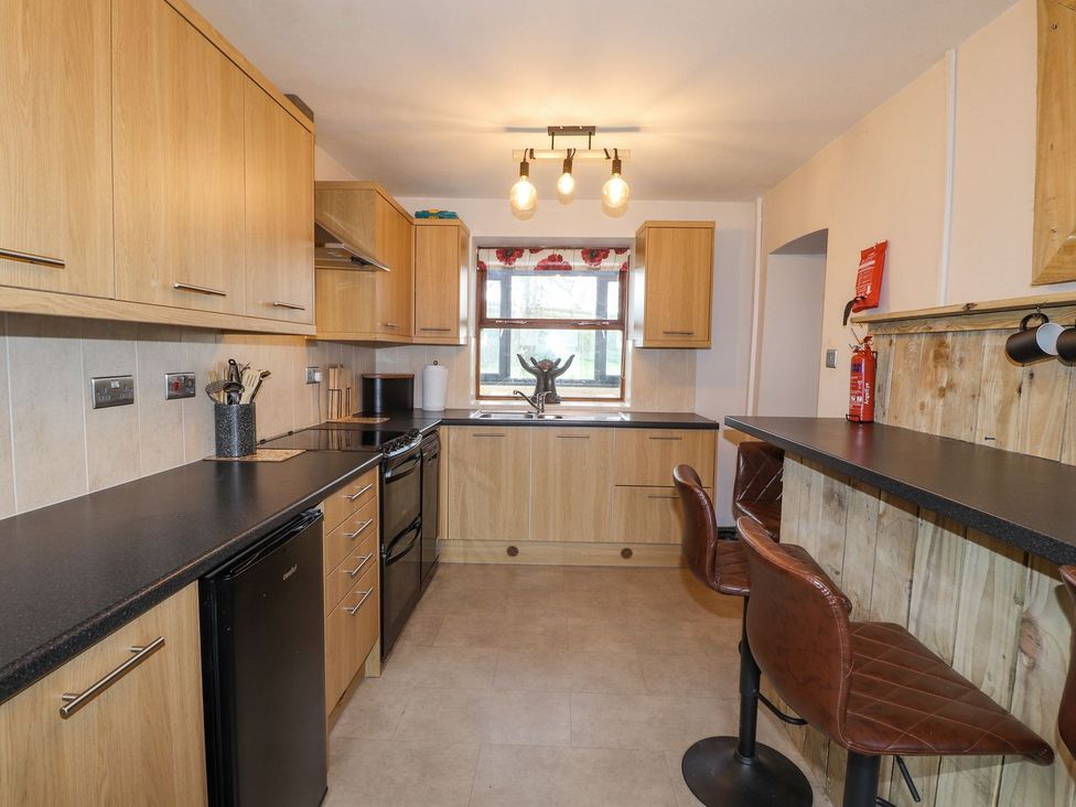 A kitchen with wood cabinets and bar stools at Clawddcam in Mathry