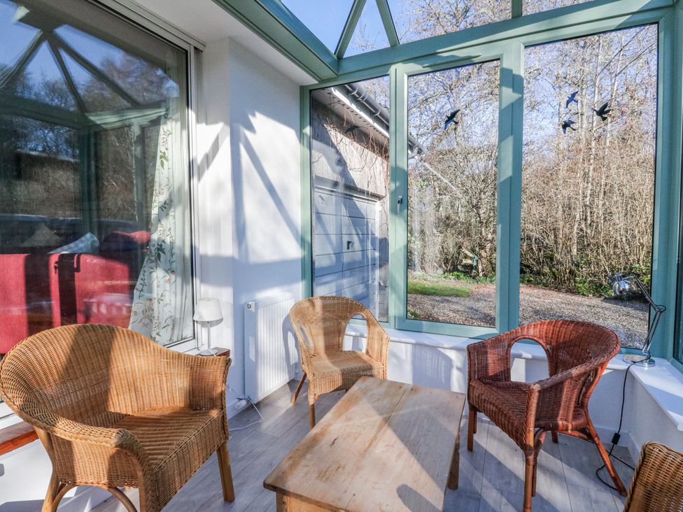 A conservatory with wicker chairs and a wooden table at Grianach near Strathtay