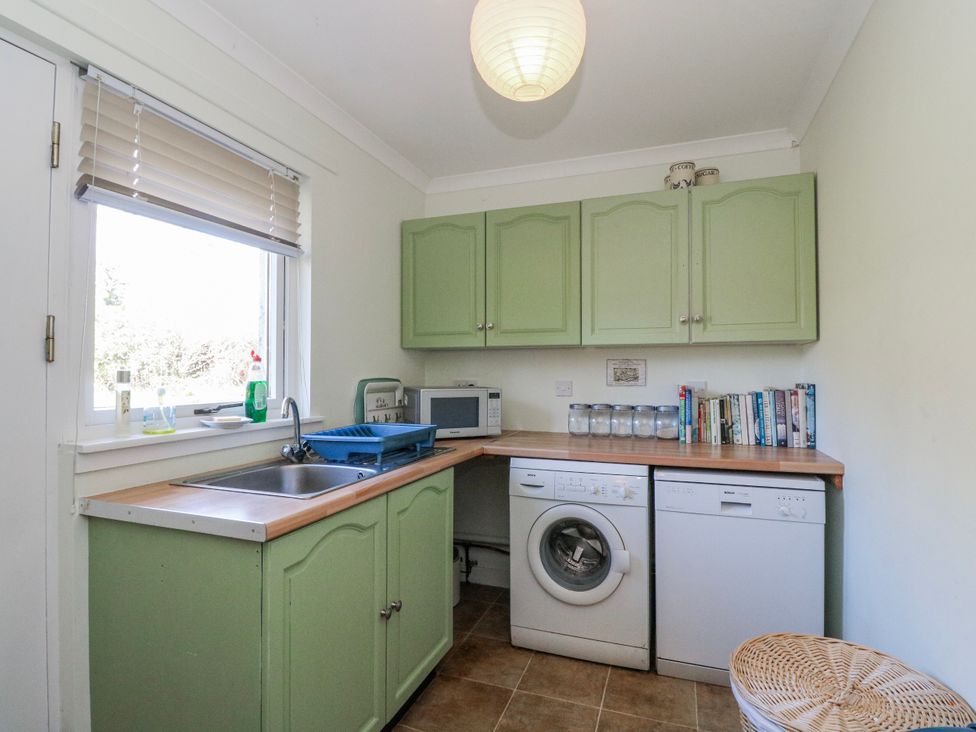 A kitchen with a sink, washing machine, and cabinets at Grianach in Balnaguard near Strathtay