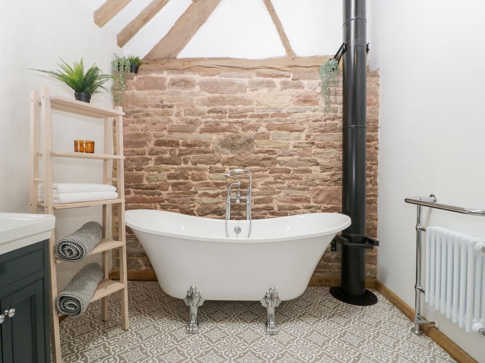 A bathroom with a bathtub and towels on a shelf at Two Parks Barn in Upton Bishop near Ross-On-Wye