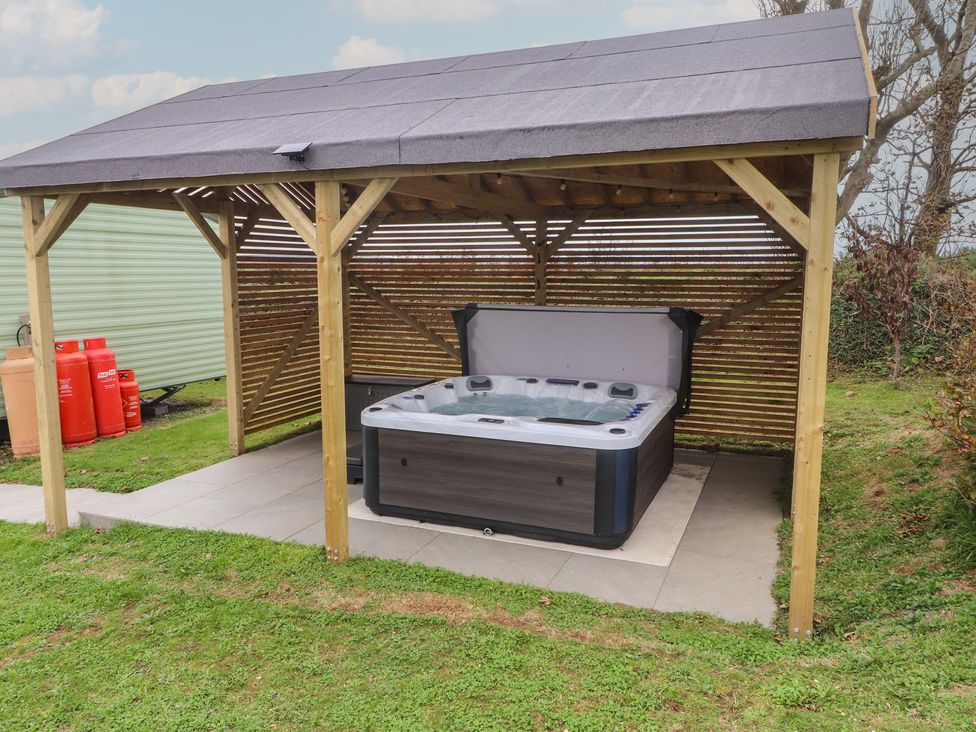 A hot tub under a wooden structure with paving stones at Bryncrin Edern near Morfa Nefyn