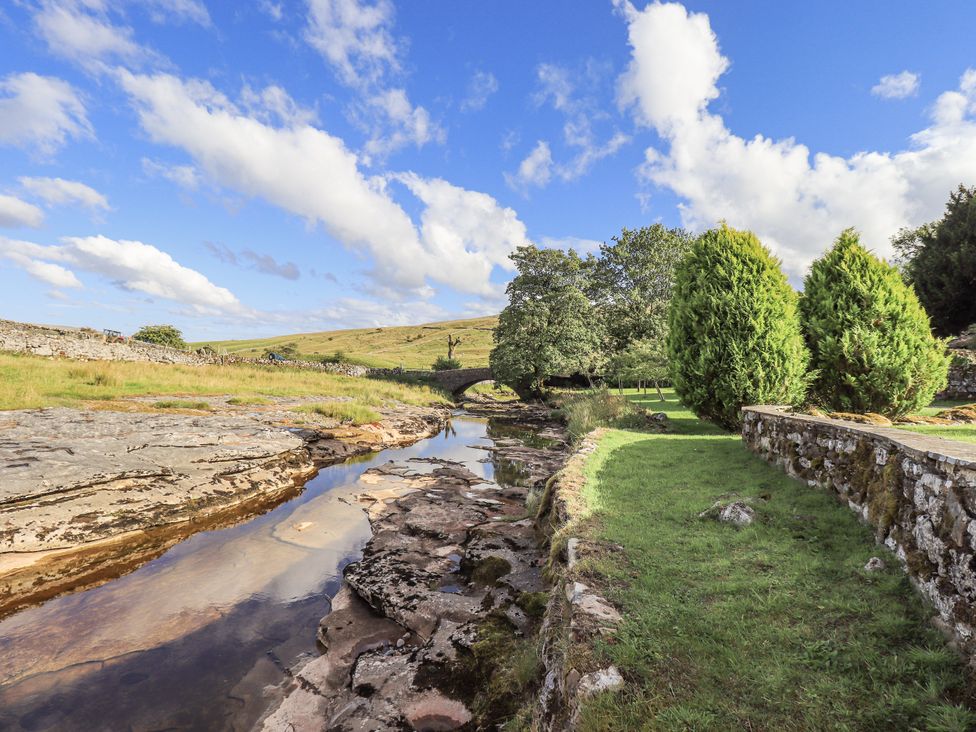 A river flowing past rocks and trees near a stone wall at Hallbeck near Kettlewell