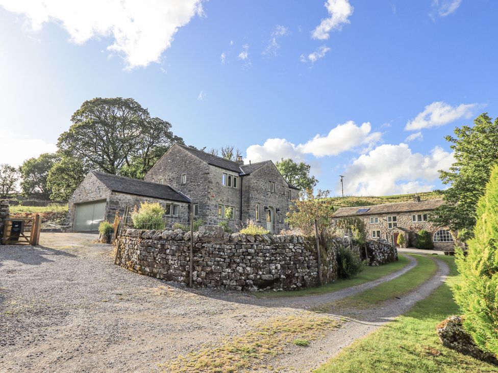 A stone house with a gravel driveway and trees at Hallbeck near Kettlewell