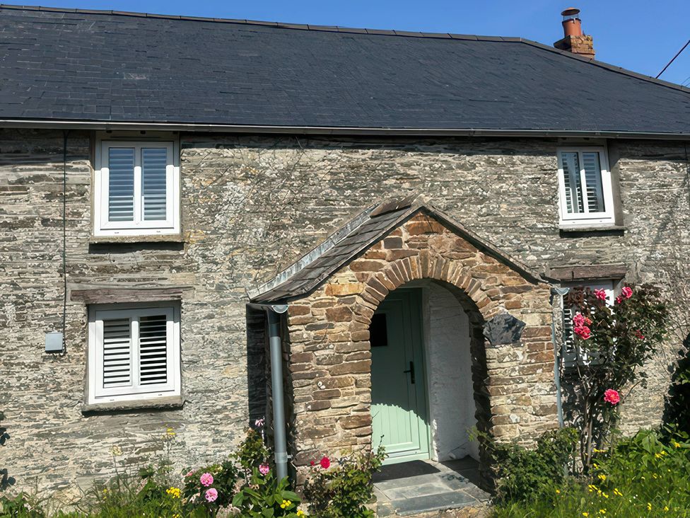 A stone house with an archway and flowers at Rose Cottage Porthcothan Bay near Padstow