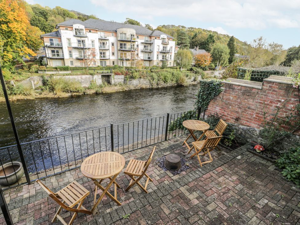 An outdoor patio with chairs and a table by a river at Bryn Dwr in Llangollen