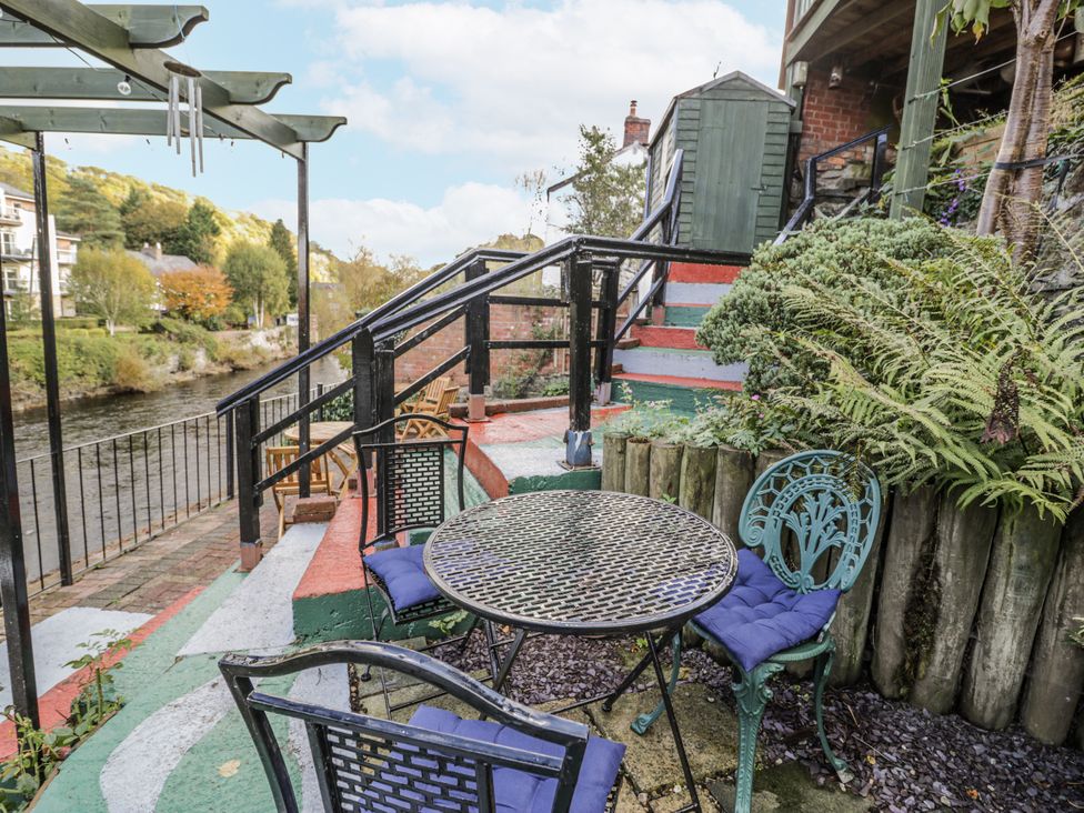 A patio with table and chairs by a river at Bryn Dwr in Llangollen