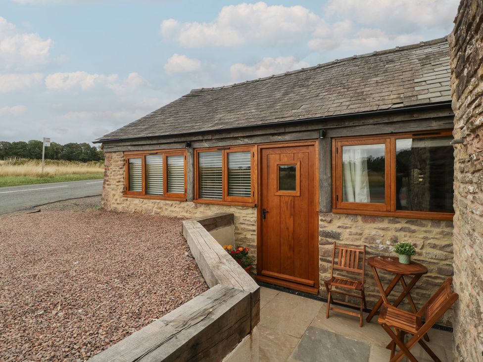 An outdoor area with a table and chairs in front of a stone building at The Old Cart Shed in Gorsley