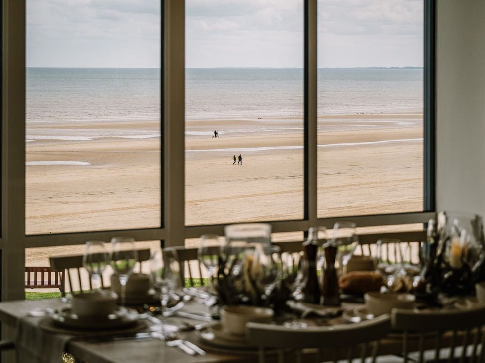 A dining room with a view of the beach and people walking at Calm Waters Luxury Beach House in Bridlington
