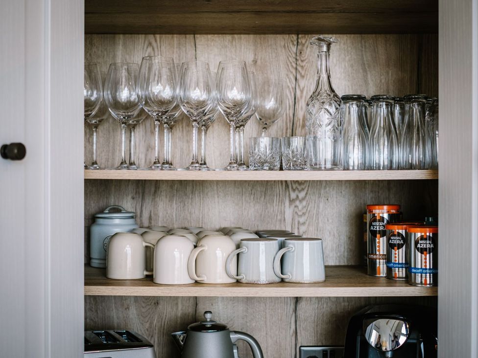 A kitchen cupboard with glassware and mugs at Calm Waters Luxury Beach House in Bridlington