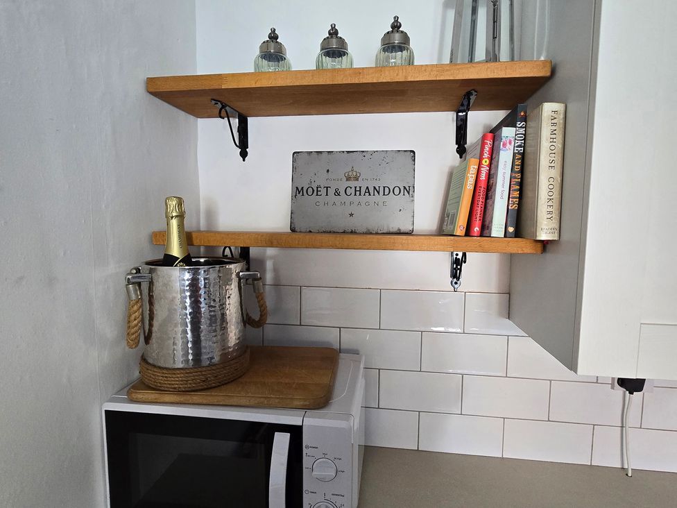 A kitchen with microwave, shelves, books, champagne bottle and ice bucket at Minns Cottage in Snainton