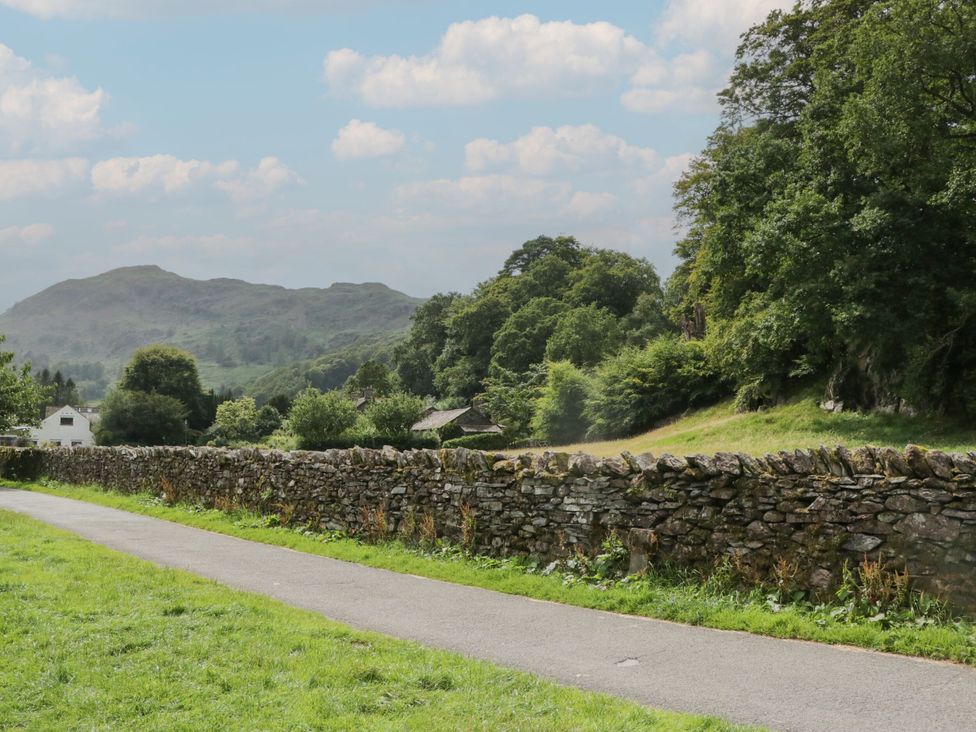 A stone wall alongside a pathway with trees and mountains at Dorothy in Ambleside