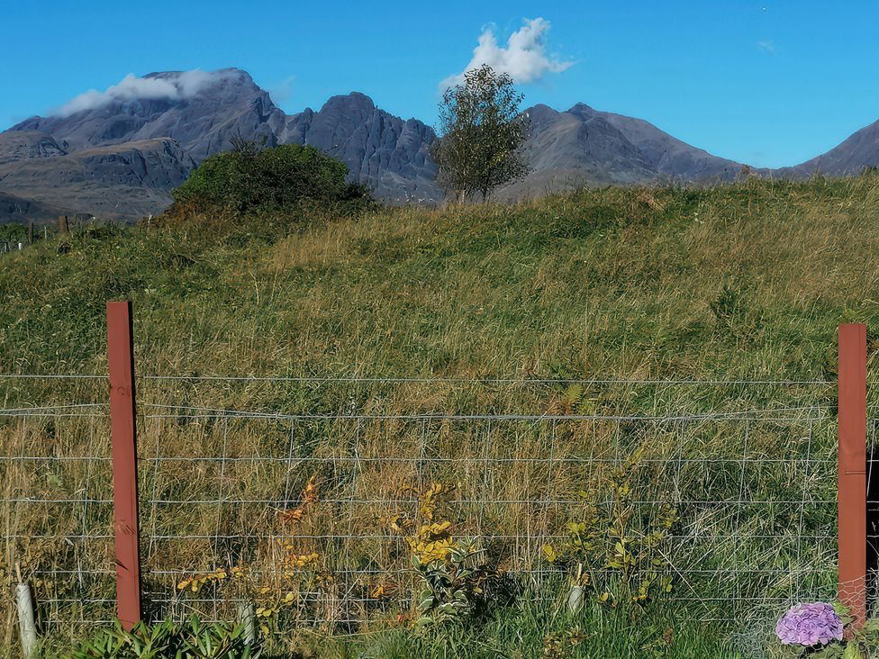 A view of mountains and grass with a fence and small flower at The Pod at Greenbank Kilbride near Broadford