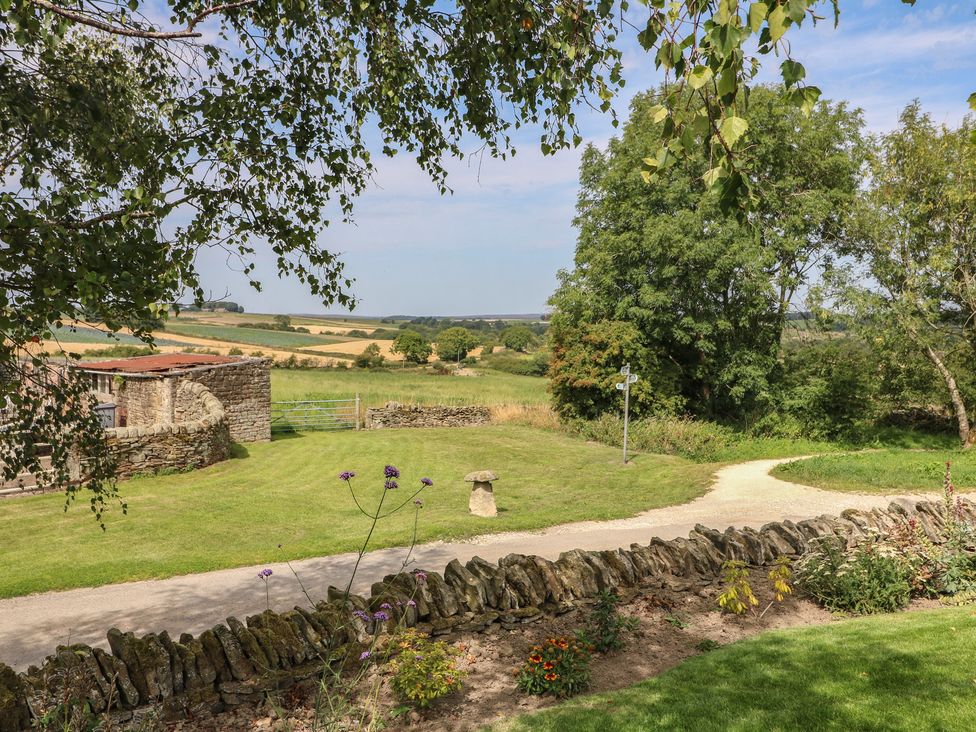 A garden view with a stone wall and trees at Wigley House Farm Bungalow Chesterfield