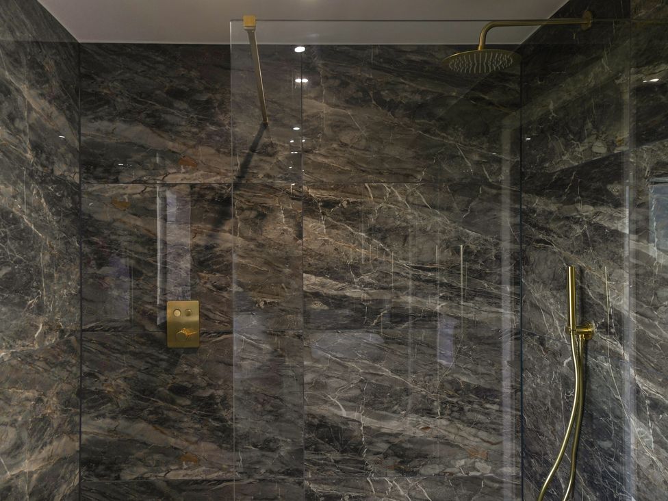 A shower with marble tiles and a gold showerhead at Northstone House Blackburn